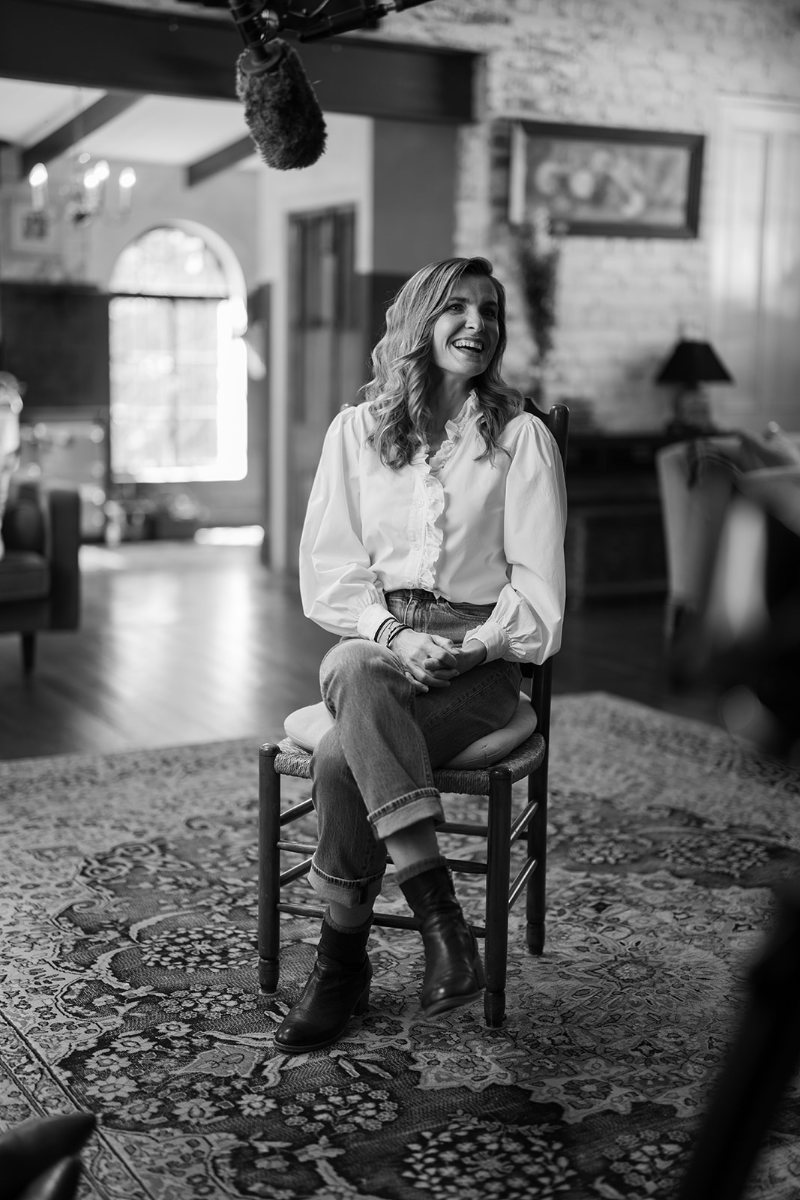 Sarah Anderson laughing, seated on a wooden chair in a sunlit room
